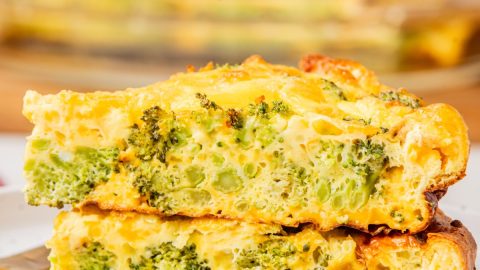 close-up shot of two slices of crustless broccoli cheddar quiche stacked on top of each other on a white plate.