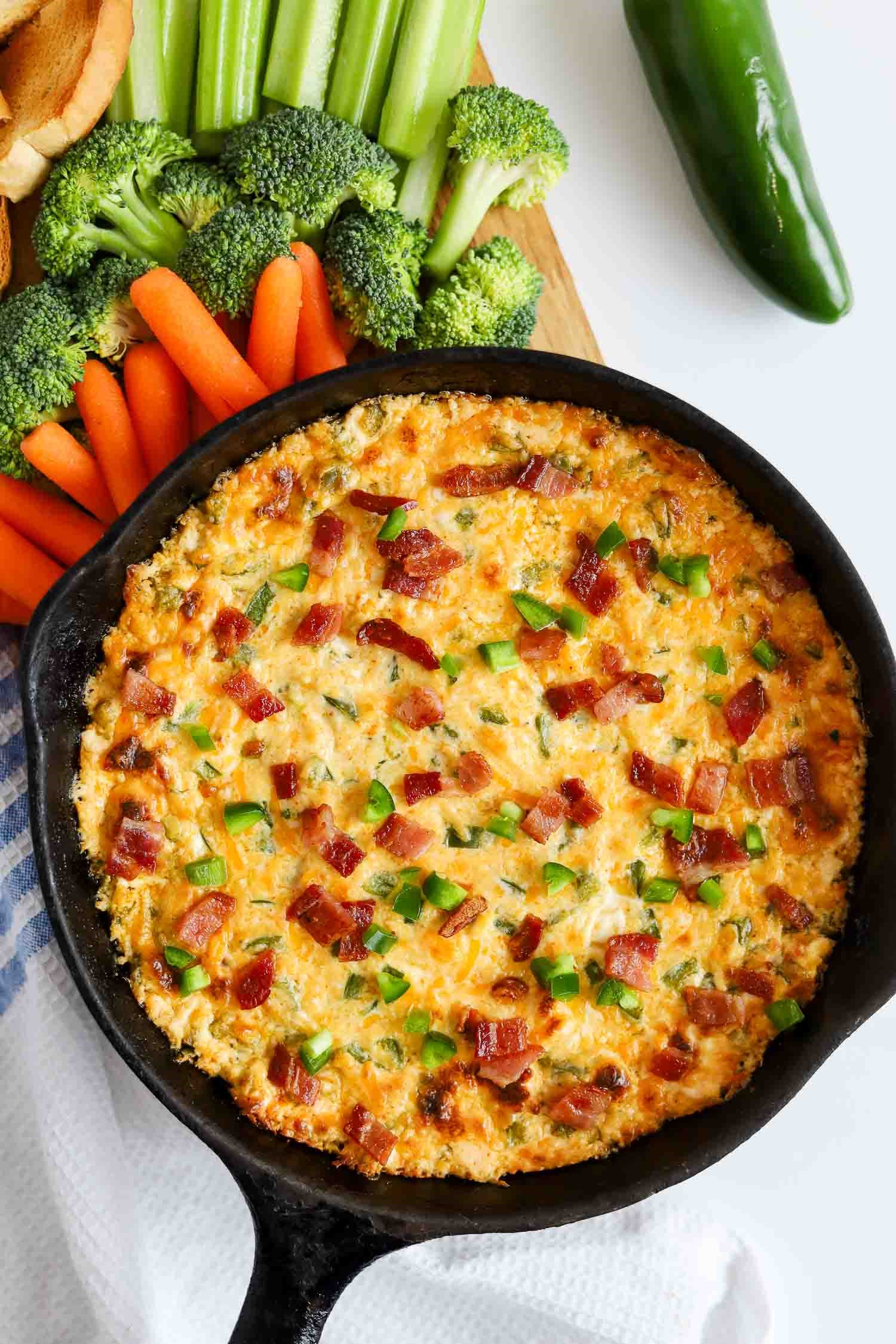 overhead of baked jalapeno popper dip in a cast iron pan with bacon crumbles and chopped jalapenos on top.