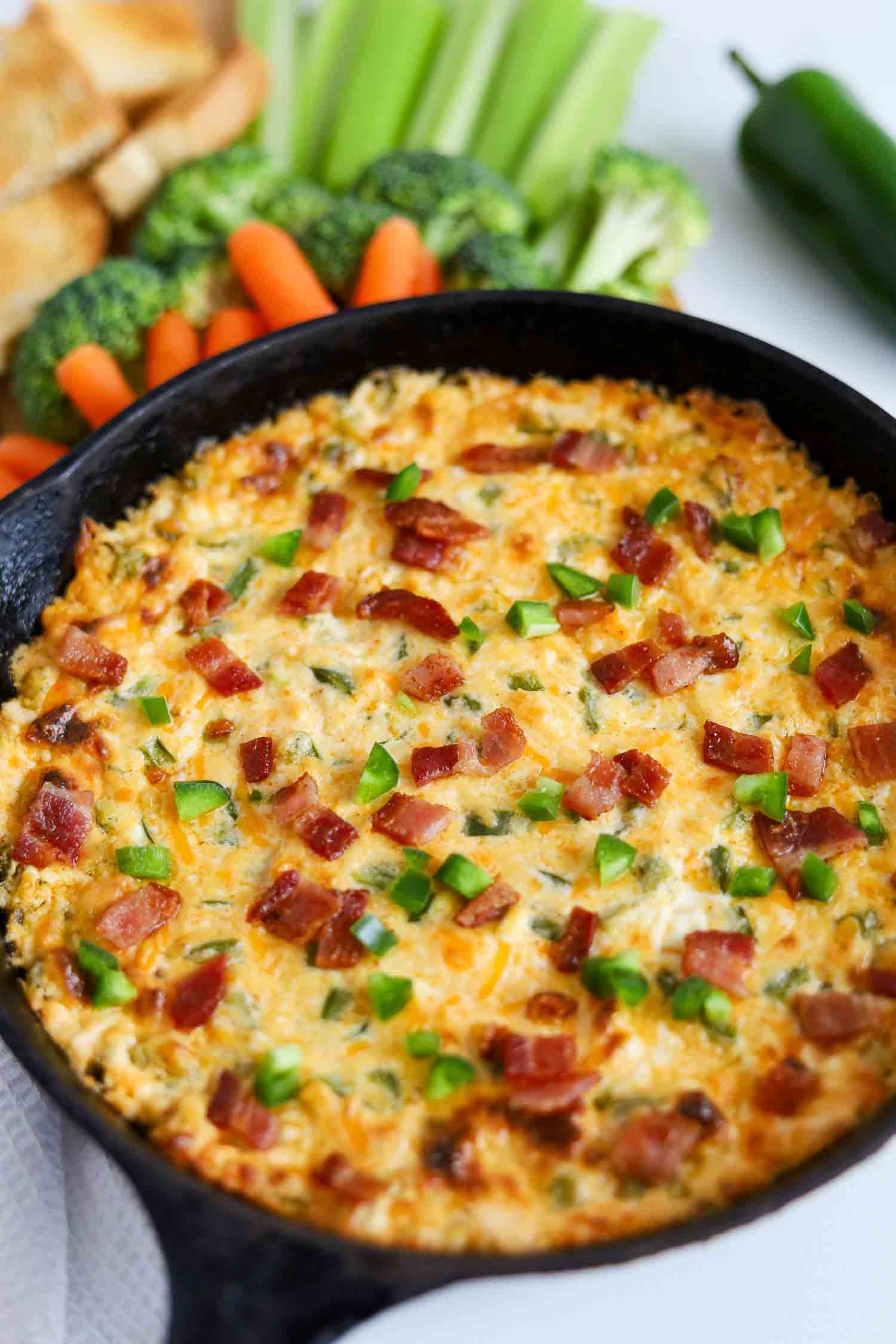 close-up of baked dip in a cast iron pan with crumbled bacon and chopped jalapenos sprinkled on top.