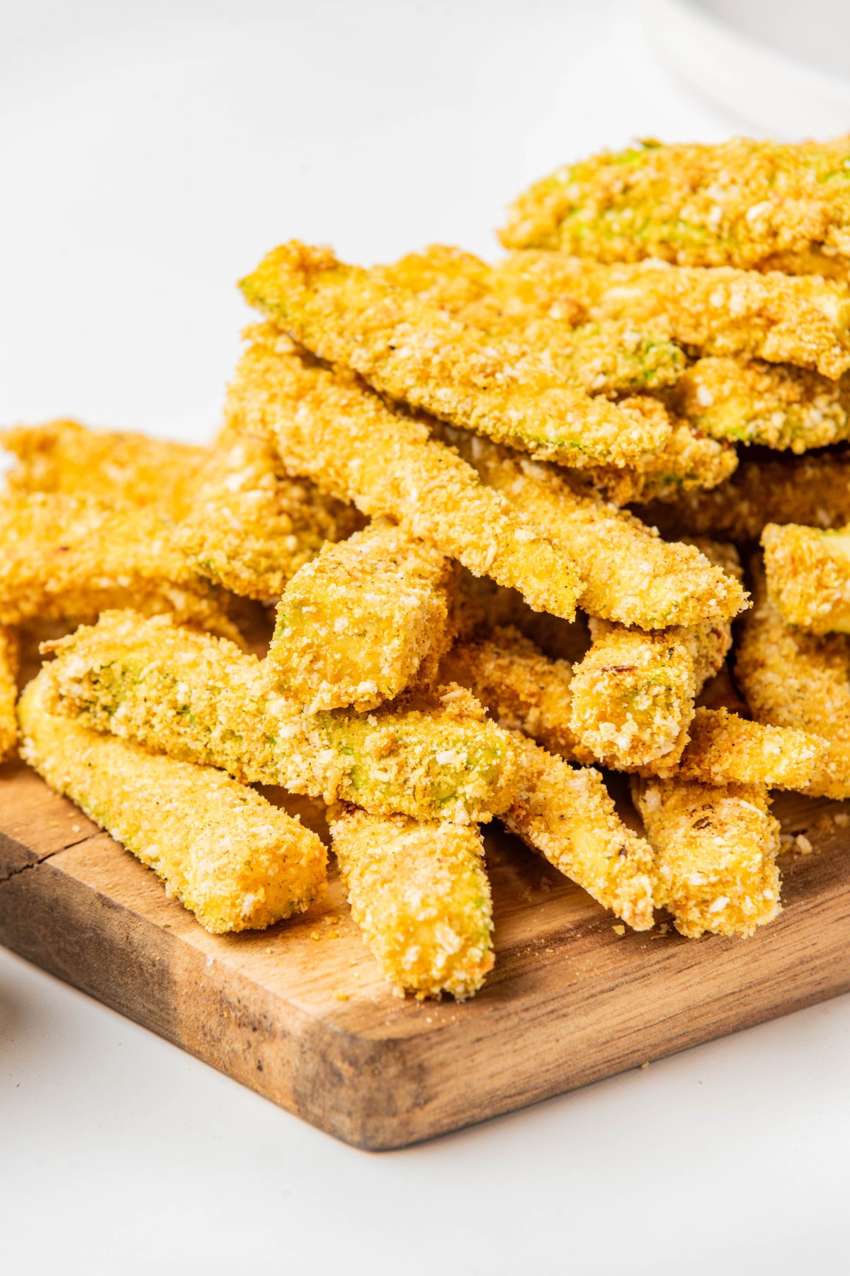 low carb zucchini fries piled on top of each other on a wooden board.