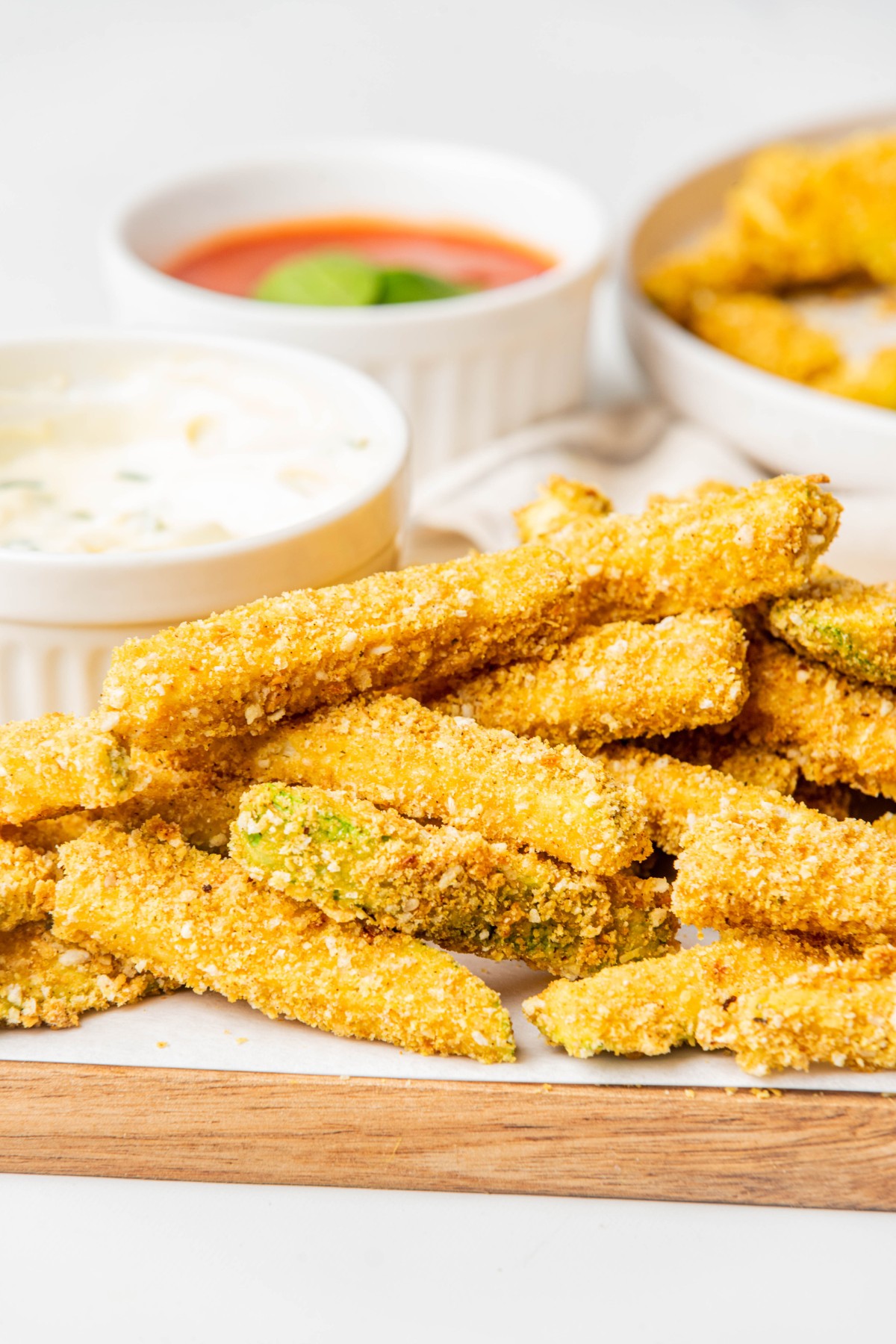 zucchini fries on a wooden board with dipping sauces in the background.
