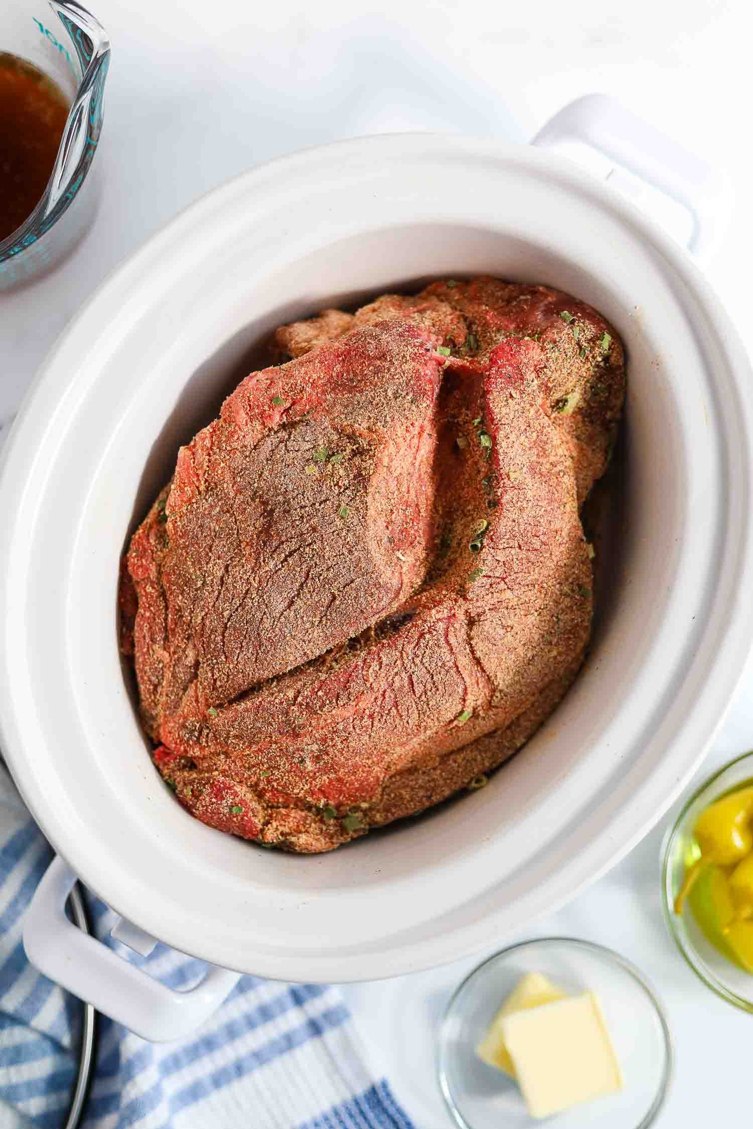 chuck roast in a crockpot with seasoning blend rubbed on it.