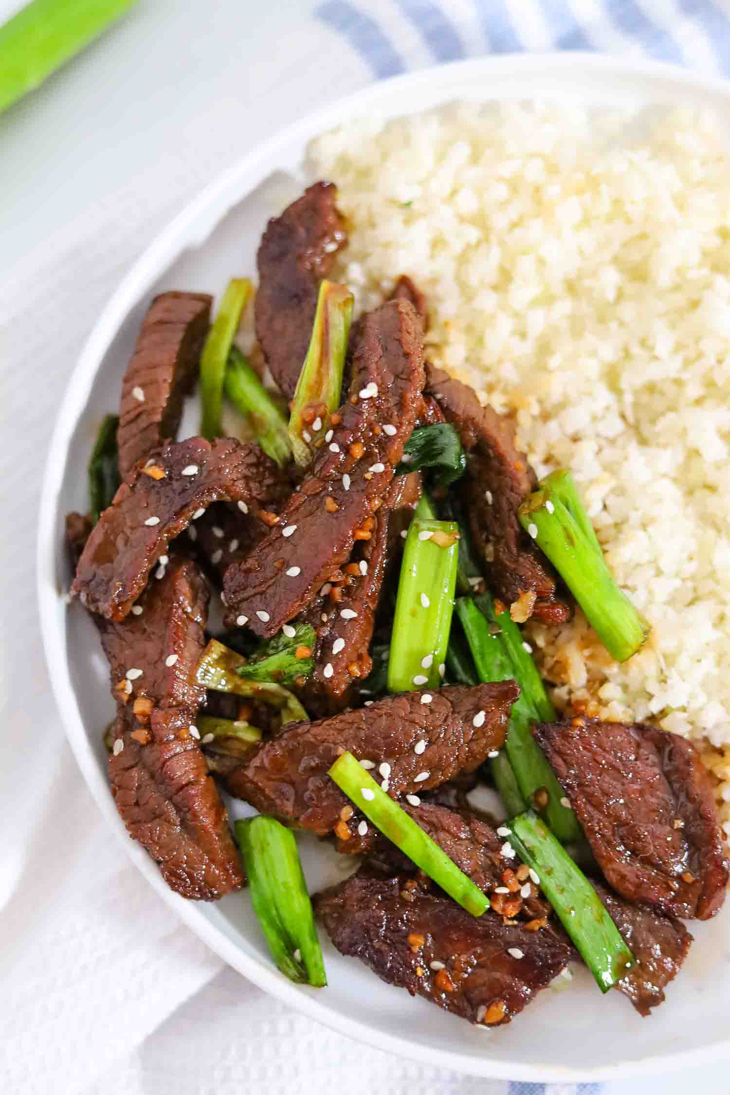 close-up shot of mongolian beef with cauliflower rice on a white plate.