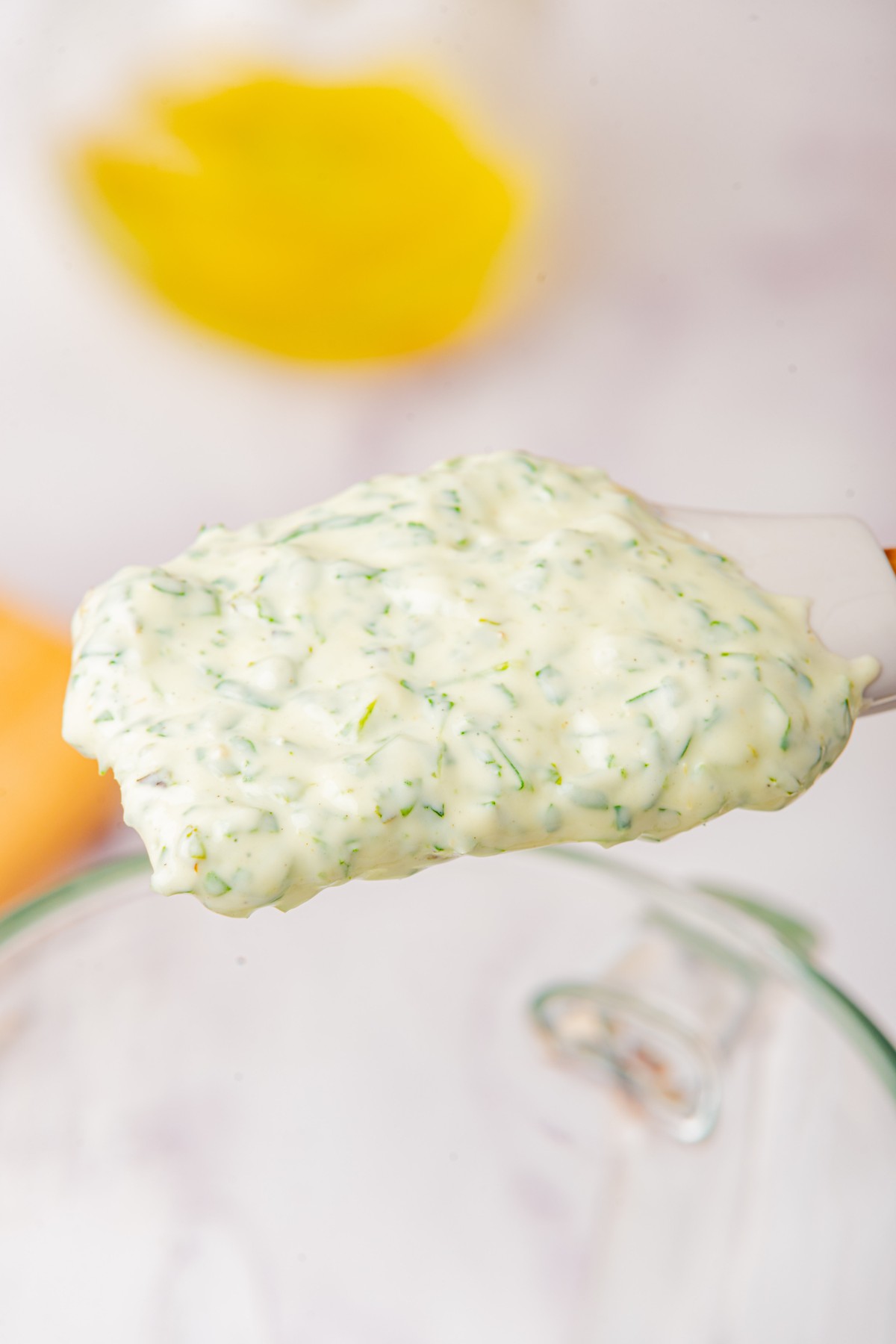 using a spatula to scoop out herb dip from blender 