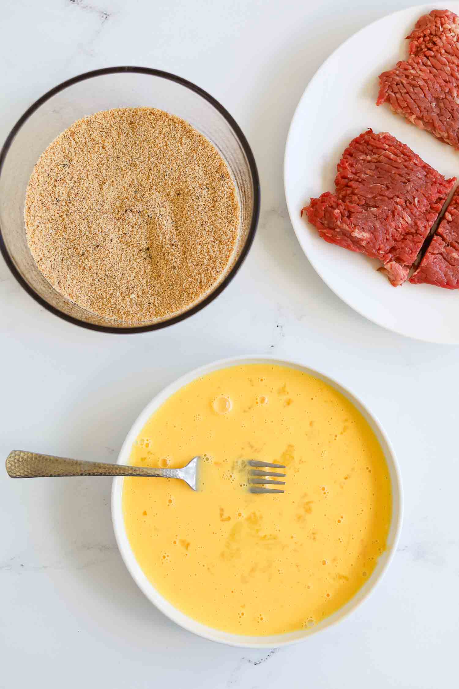 beaten eggs in a white bowl with bread crumbs. 