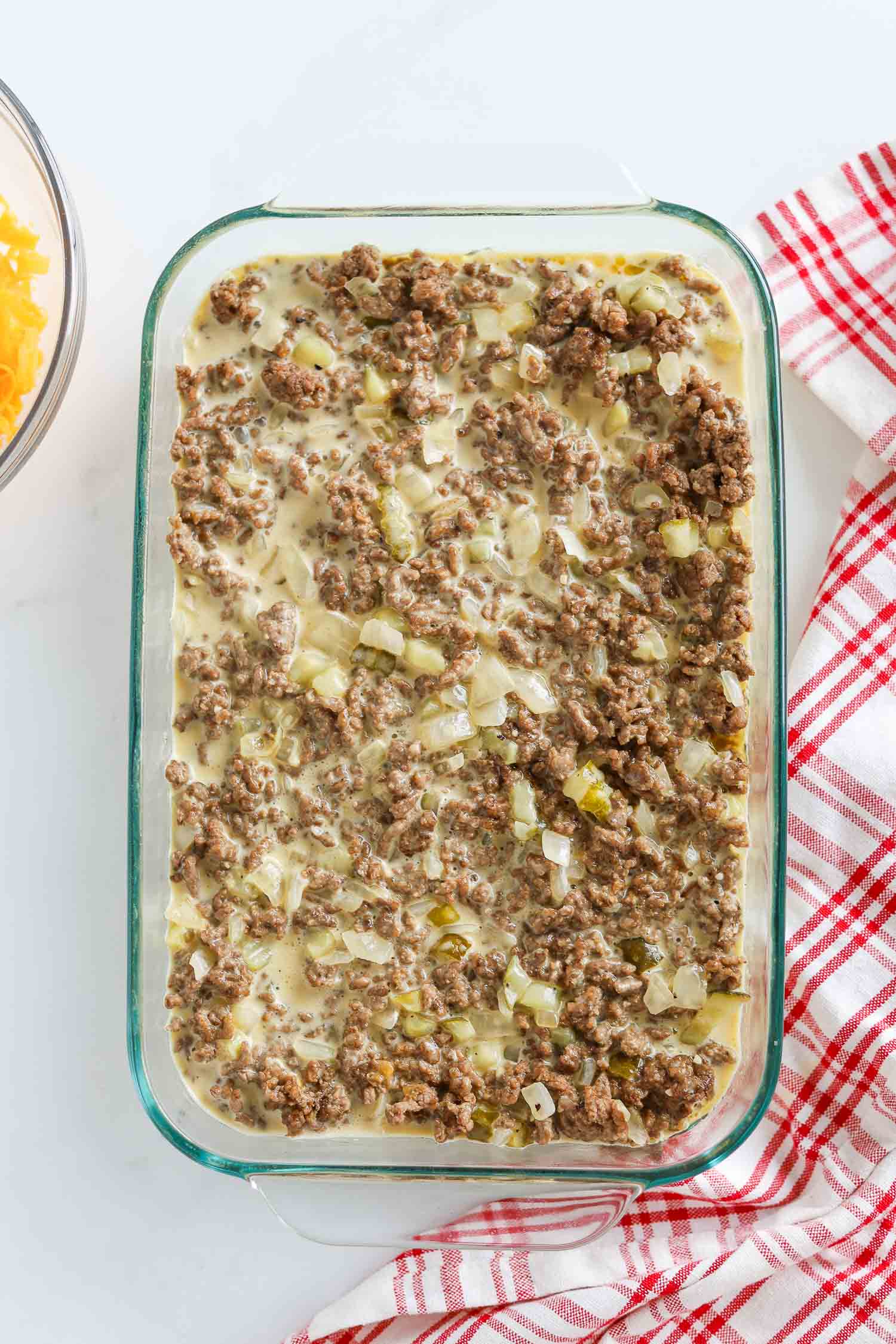 adding ground beef to casserole pan with egg mixture