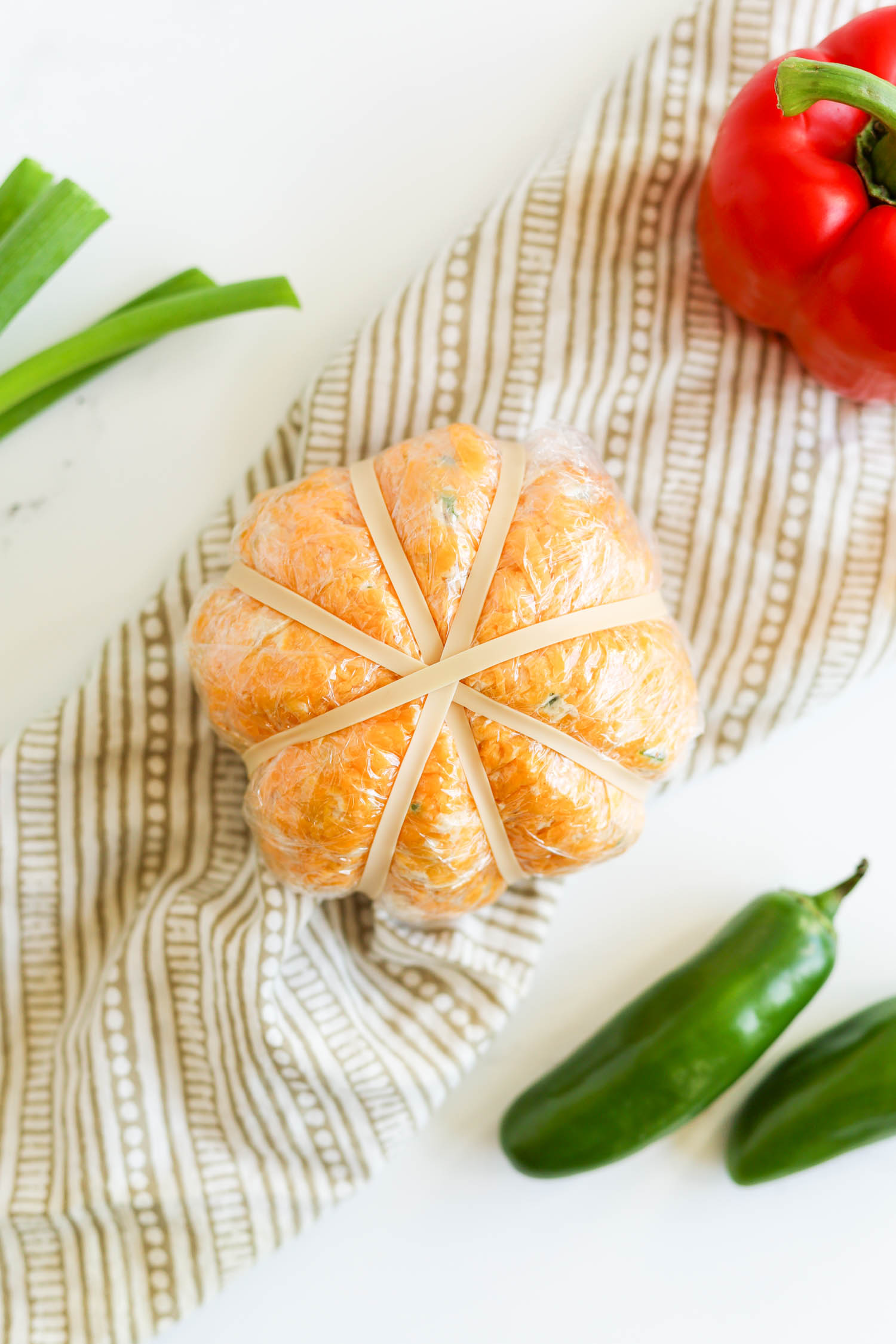 cheese ball wrapped in plastic and rubber bands to make pumpkin shape