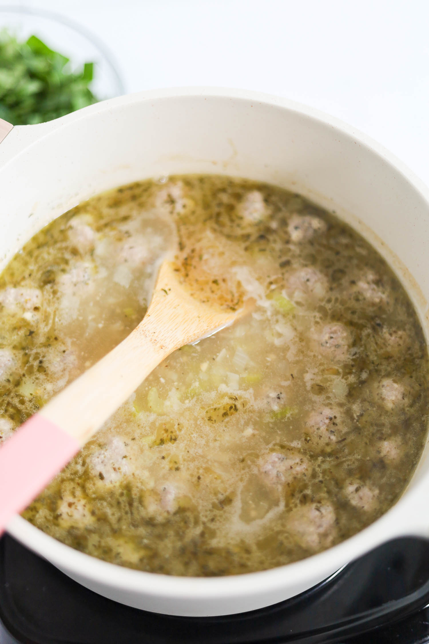 adding raw meatballs to chicken broth and veggies in a soup pot 